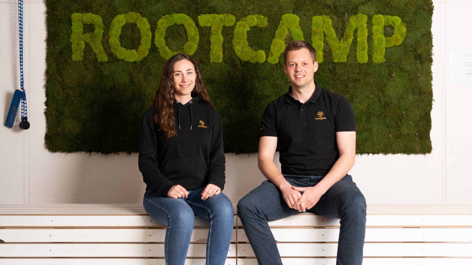 A photo of the founders of Artenglück with the RootCamp Logo in the background