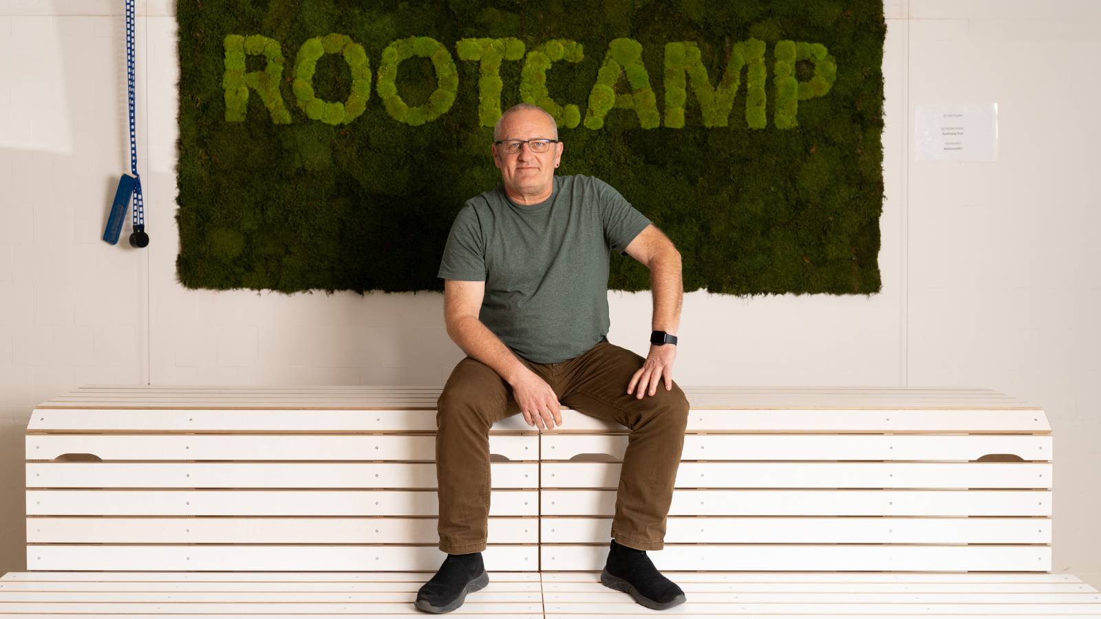 founder jens of seedalive in the rootcamp office sitting on stairs and in the background a rootcamp moss wall in green