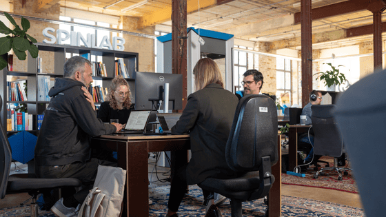 a photo of 4 people sitting on a desk in a office and working 